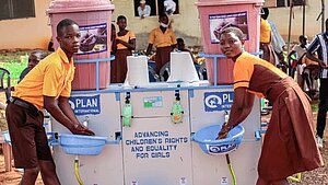 Schüler und Schülerin in Ghana waschen sich an einer mobilen Station von Plan International die Hände
