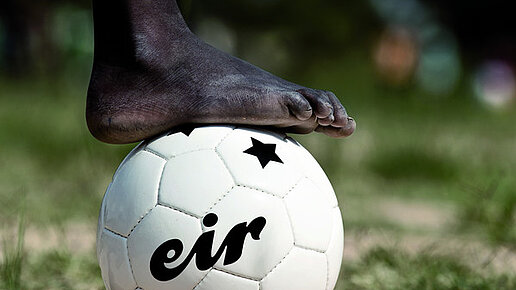 Ein Fußball liegt auf einer Wiese und eine Person hat ihren Fuß darauf gestellt.