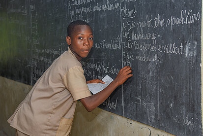 Ein Junge schreibt mit Kreide an eine Tafel