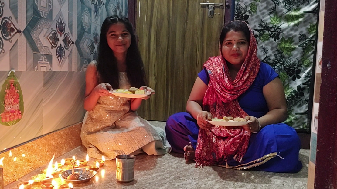 Ein Mädchen und eine Frau sitzen im Schneidersitz auf dem Boden. Vor ihnen stehen Kerzen und Essen auf Tellern.