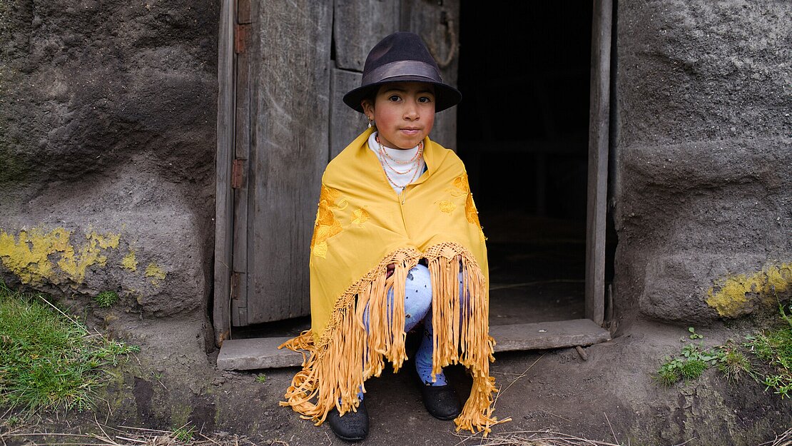 Ein Mädchen mit einem gelben Poncho sitzt in der Tür einer Hütte