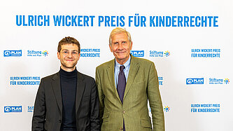 Anton Stanislawski steht neben Ullrich Wickert vor einem Hintergrund, auf dem "Ulrich Wickert Preis für Kinderrechte" steht