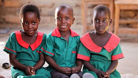 Bild: Drei kleine Kinder sitzen auf einer Bank in einer Schule