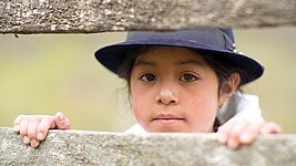Ein kleines Mädchen guckt durch einen Zaun ernst in die Kamera © Plan International / Verité