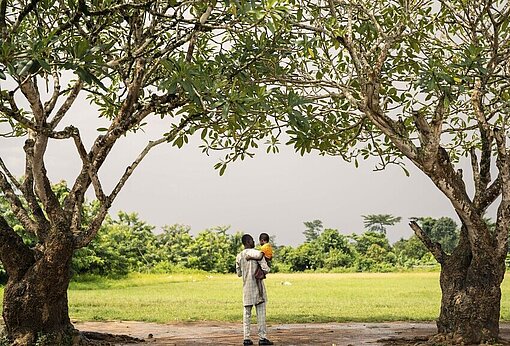 Ein Vater trägt seine Tochter durch eine Allee aus Bäumen.