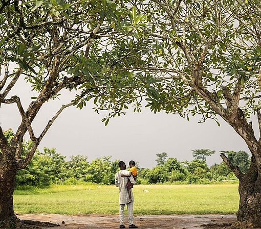 Ein Vater trägt seine Tochter durch eine Allee aus Bäumen.