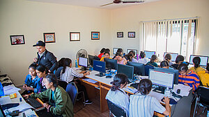Junge Frauen in Nepal nehmen an einem Computerkurs in einem Schulungsraum teil, unterstützt von einem Ausbilder