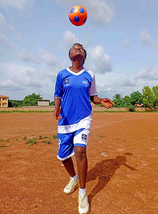 Ein Mädchen mit Fußballtrikot kickt einen Ball in die Luft