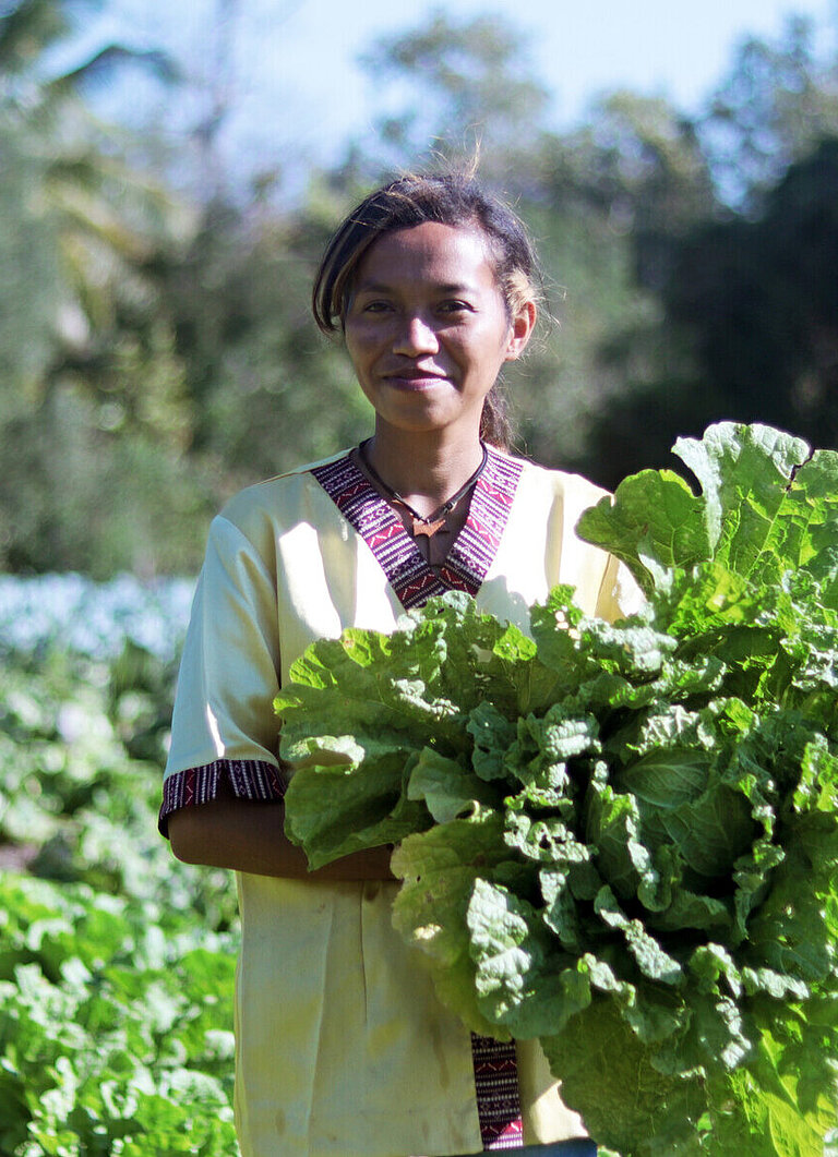 Eine junge Frau steht auf einem Feld und hält einen großen Kohl in der Hand