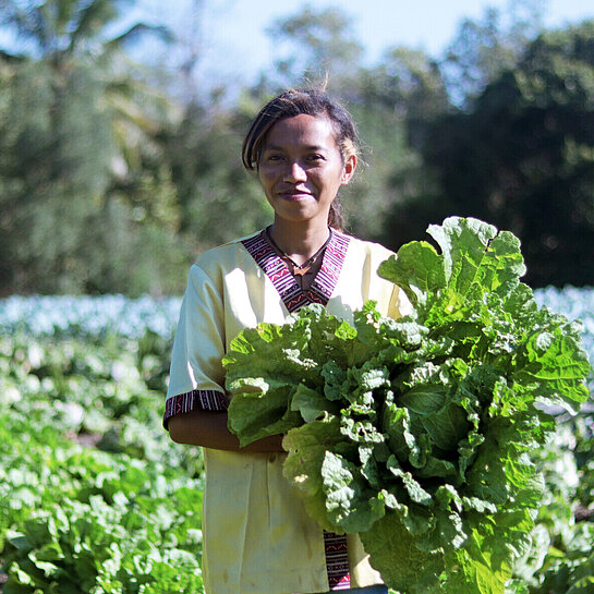 Eine junge Frau steht auf einem Feld und hält einen großen Kohl in der Hand