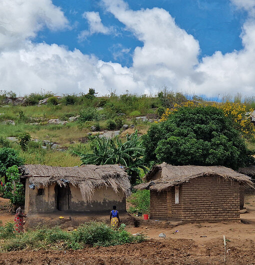 Lehmhäuser mit Strohdächern in einem Dorf in Malawi vor grünen Hügeln.
