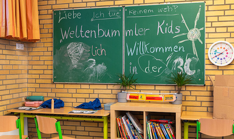 Klassenraum einer Grundschule mit Tafelaufschrift „Weltenbummler Kids – Willkommen in der 3c“