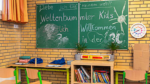 Klassenraum einer Grundschule mit Tafelaufschrift „Weltenbummler Kids – Willkommen in der 3c“