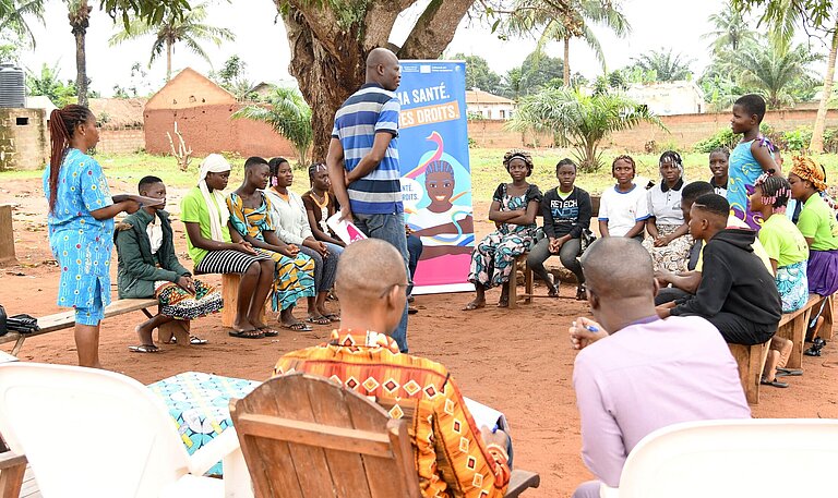 Junge Menschen mit Lehrenden sitzen draußen im Kreis und nehmen an einer Schulung teil