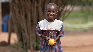 Lächelndes Mädchen in Ghana hält eine Frucht in der Hand und steht auf einem Dorfweg
