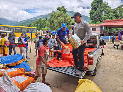 Verteilung von Hilfsgütern durch Plan International: Menschen erhalten Lebensmittel und Versorgungspakete vom Pickup in Nepal nach einer Flutkatastrophe.