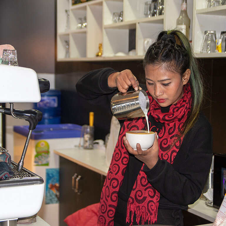 Eine junge Frau gießt geschäumte Milch in eine Kaffeetasse