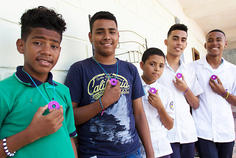Fünf Jungen haben einen Menstruationstracker um den Hals hängen und halten ihn jeweils mit einer Hand fest