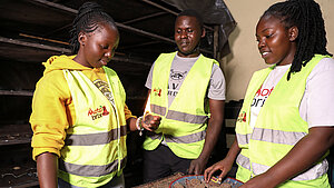 Mitglieder der Motobrix-Initiative produzieren nachhaltige Feueranzünder aus recyceltem Abfall in Nairobi. Drei junge Mitglieder der Motobrix-Initiative in Nairobi testen nachhaltige Feueranzünder aus lokalem Abfall in einem Produktionsraum.