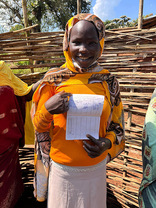 Projektteilnehmerin zeigt ihre handschriftliche Buchführung zur Unternehmensgründung vor einem geflochtenen Holzzaun in Äthiopien