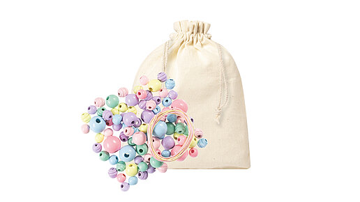 Baumwollbeutel, darauf liegen pastellfarbene Holzperlen und Kordeln.