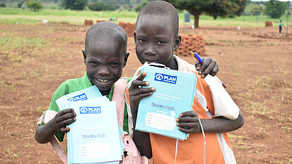 Zwei Jungen sind glücklich und zeigen ihre Schreibhefte, die zuvor verteilt wurden.