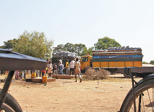 Auf einem sandigen Dorfplatz stehen zwei Lastwagen