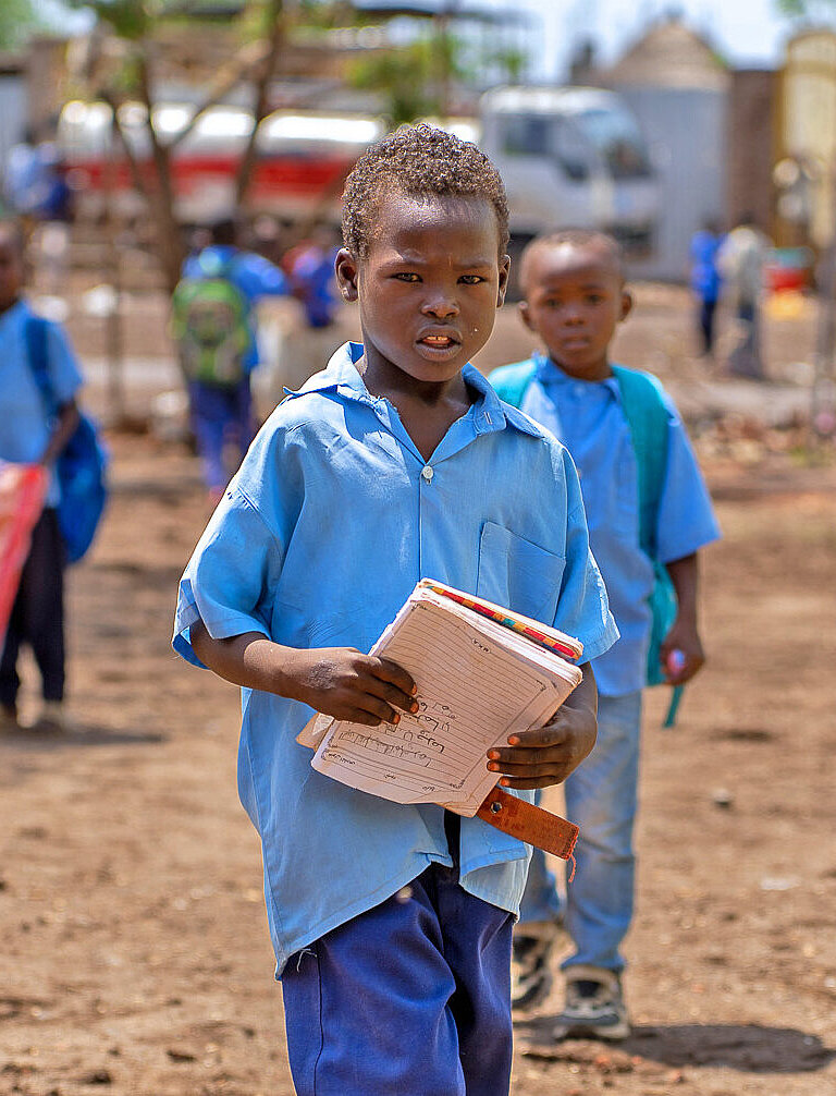 Ein Junge in blauer Hose und blauem Hemd trägt Schulbücher