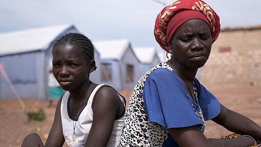 Mutter und Tochter sitzen gemeinsam vor Geflüchtetencamp in Burkina Faso Tochter Justine sitzt mit ihrer Mutter Bibata Rücken an Rücken vor ihrem Zelt