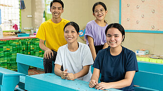 Vier jugendliche Peer-Educator:innen sitzen in einem Klassenraum mit hellblauen Tischen und Bänken. 