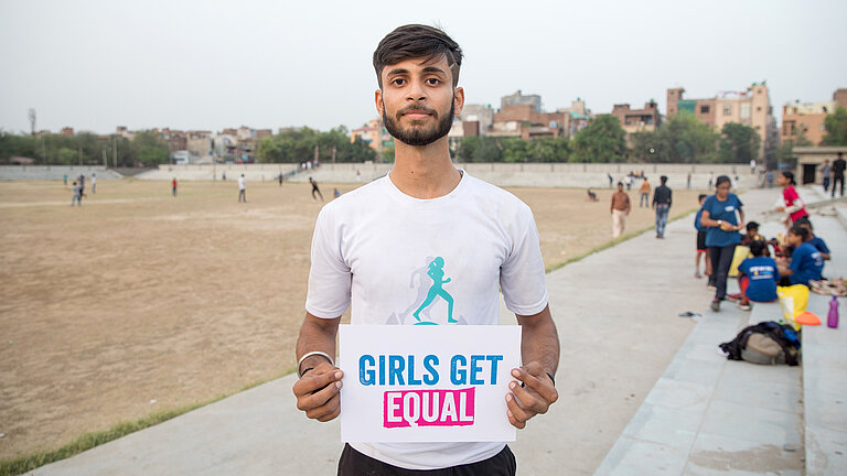 Kushal auf einem Sportplatz hält ein Girls Get Equal Schild.