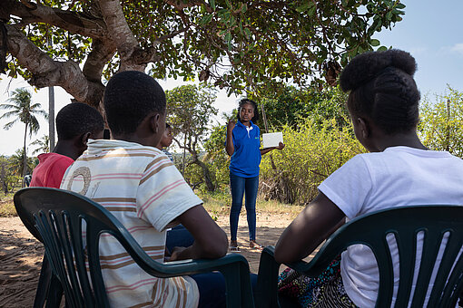 Eunice diskutiert mit anderen Aktivist:innen, die vor ihr auf Plastikstühlen sitzen