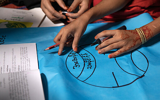 Nahaufnahme von Kinderhänden, die auf einem Schulplakat schreiben