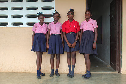 Vier Mädchen in Schuluniformen stehen vor einer Schule