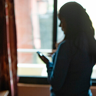 Im Gegenlicht ist die Silhouette einer jungen Frau in einem Zimmer zu erkennen