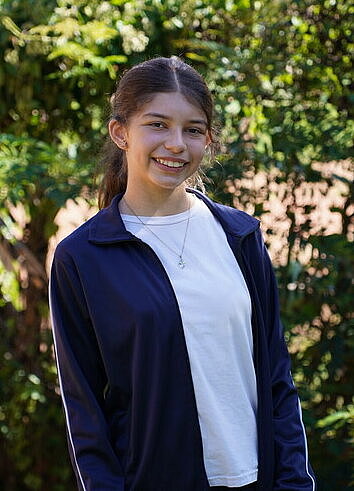 Ein Mädchen steht in einem Garten und lächelt breit.