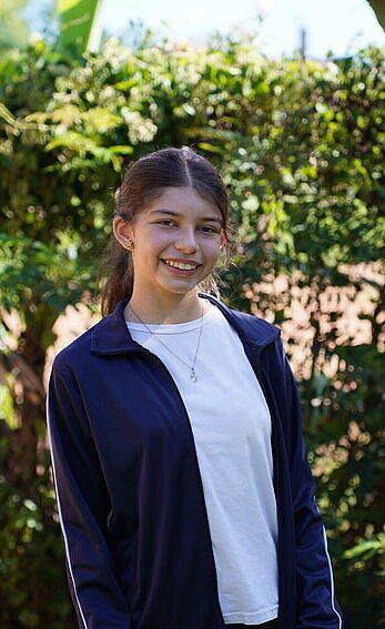 Ein Mädchen steht in einem Garten und lächelt breit.