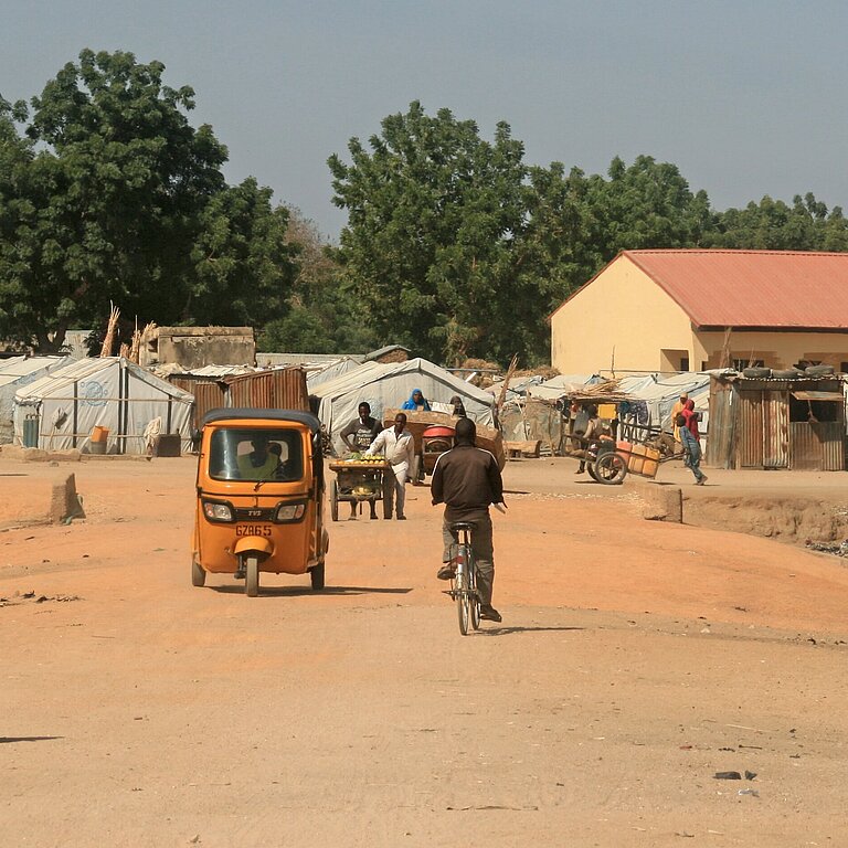 Momentaufnahme Menschen im Dorf mit Fahrzeugen