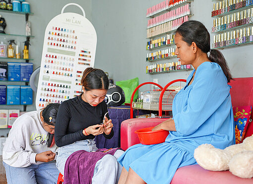 Zwei junge Asiatinnen hocken vor einer dritten asiatischen Frau