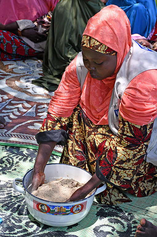 Eine Frau sitzt auf den Knien und mixt mit ihren Händen Mehl in einem Topf