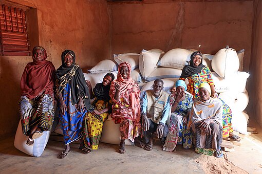 Eine Gruppe Frauen in bunten Gewändern und ein Mann vor Getreidesäcken