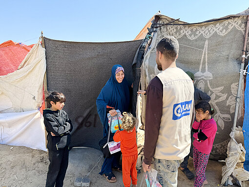 Geflüchtete Familie erhält Hilfsgüter von Plan International Mitarbeitendem in provisorischem Zeltlager in Gaza