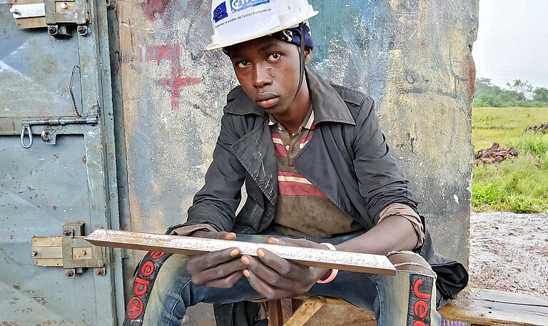 Ein junger Mann sitzt vor einer Werkstatt in Guinea