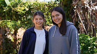 Zwei Mädchen im Teenageralter stehen Schulter an Schulter und lächeln.