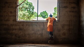 Ein Mädchen schaut aus dem Fenster hinaus. Es steht mit dem Rücken zur Kamera.