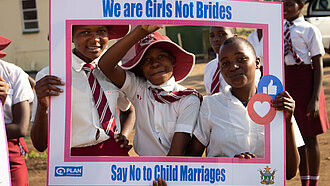 Schulmädchen in Uniform halten Schild mit der Aufschrift „We are Girls Not Brides – Say No to Child Marriages“ und setzen sich gegen Kinderheirat ein