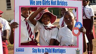 Schulmädchen in Uniform halten Schild mit der Aufschrift „We are Girls Not Brides – Say No to Child Marriages“ und setzen sich gegen Kinderheirat ein