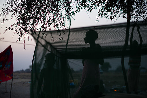 Ein Teenager-Mädchen steht vor einem Moskitonetz, es sind nur ihre Umrisse zu sehen