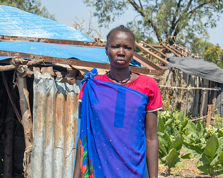 Eine junge Frau steht vor einer Wellblechhütte in Südsudan