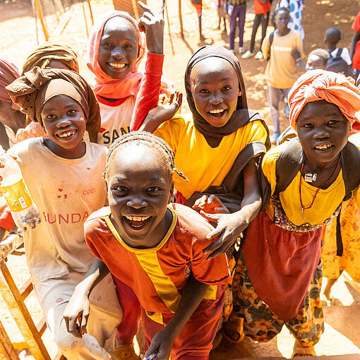 Kinder im Geflüchtetencamp im Sudan steigen eine Treppe hinauf. Sie nehmen an Nothilfe- und Bildungsprojekten von Plan International teil, die Zugang zu Schutz, Versorgung und Unterricht bieten.